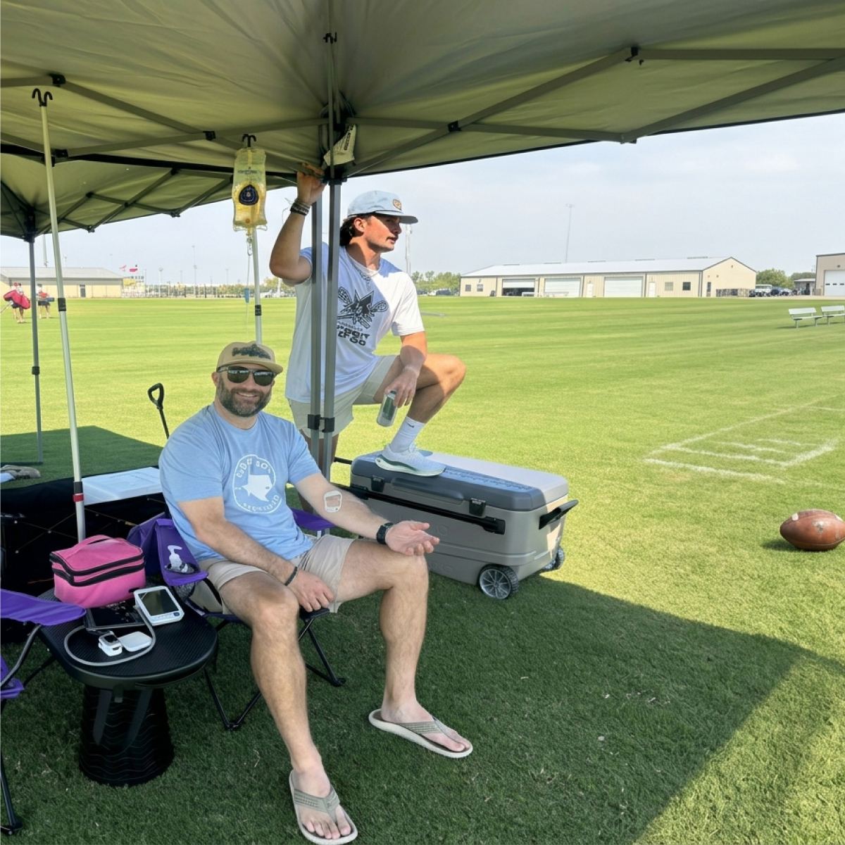 Two clients under a tent on a sports field during their IVs
